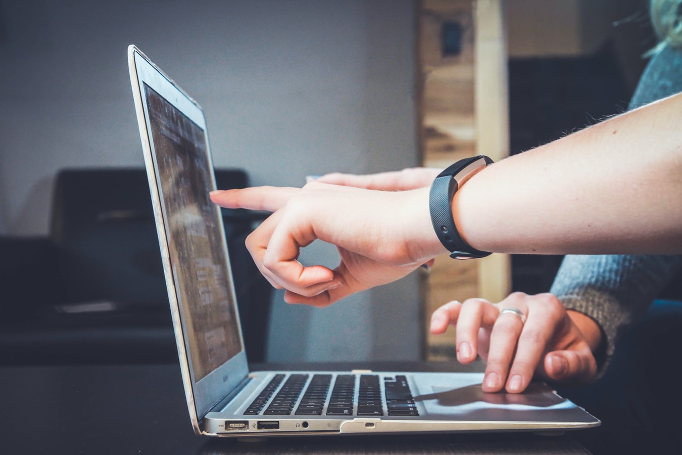 A laptop with two people pointing at the screen.